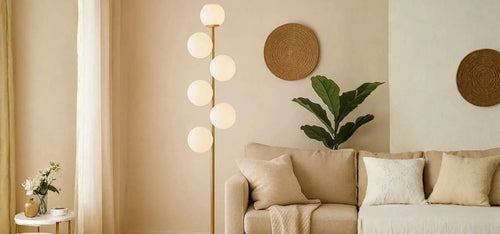 Minimal σαλόνι με καναπέ, επιδαπέδιο φωτιστικό με σφαιρικά φωτιστικά σώματα και φυτά εσωτερικού χώρου σε ζεστή ατμόσφαιρα.