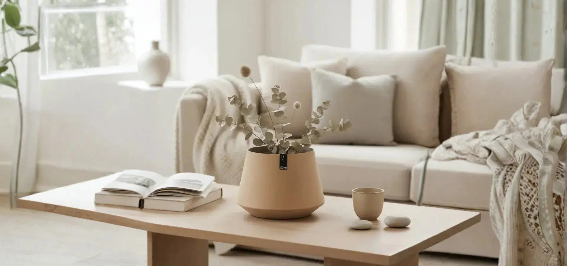 Minimal σαλόνι με ουδέτερες αποχρώσεις, διακοσμητικά μαξιλάρια και κεραμικό βάζο πάνω σε ξύλινο τραπεζάκι σαλονιού.