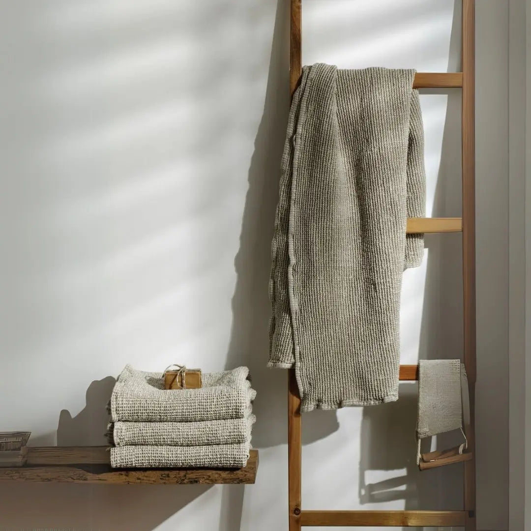 Η πετσέτα Waffled Linen κρεμασμένη σε ξύλινη σκάλα δίπλα σε διπλωμένες πετσέτες